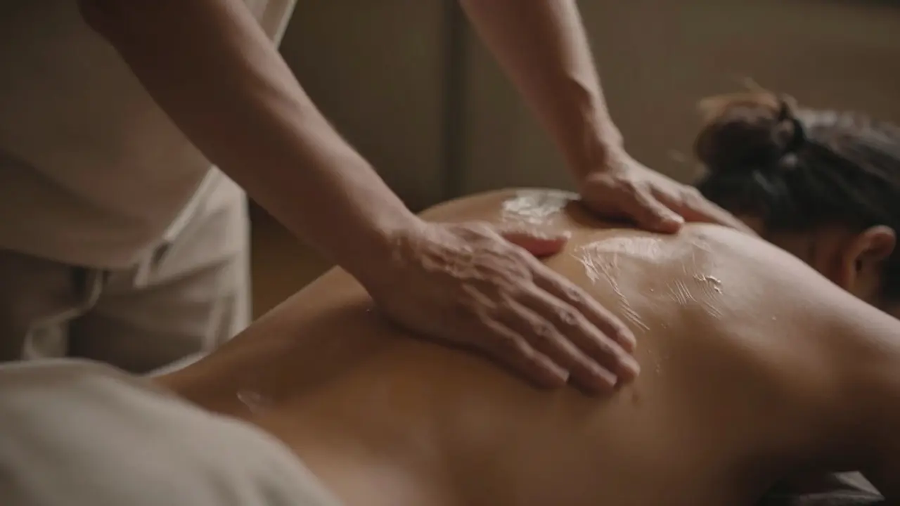 Therapist using forearm strokes for Lomi Lomi massage in a dimly lit room.